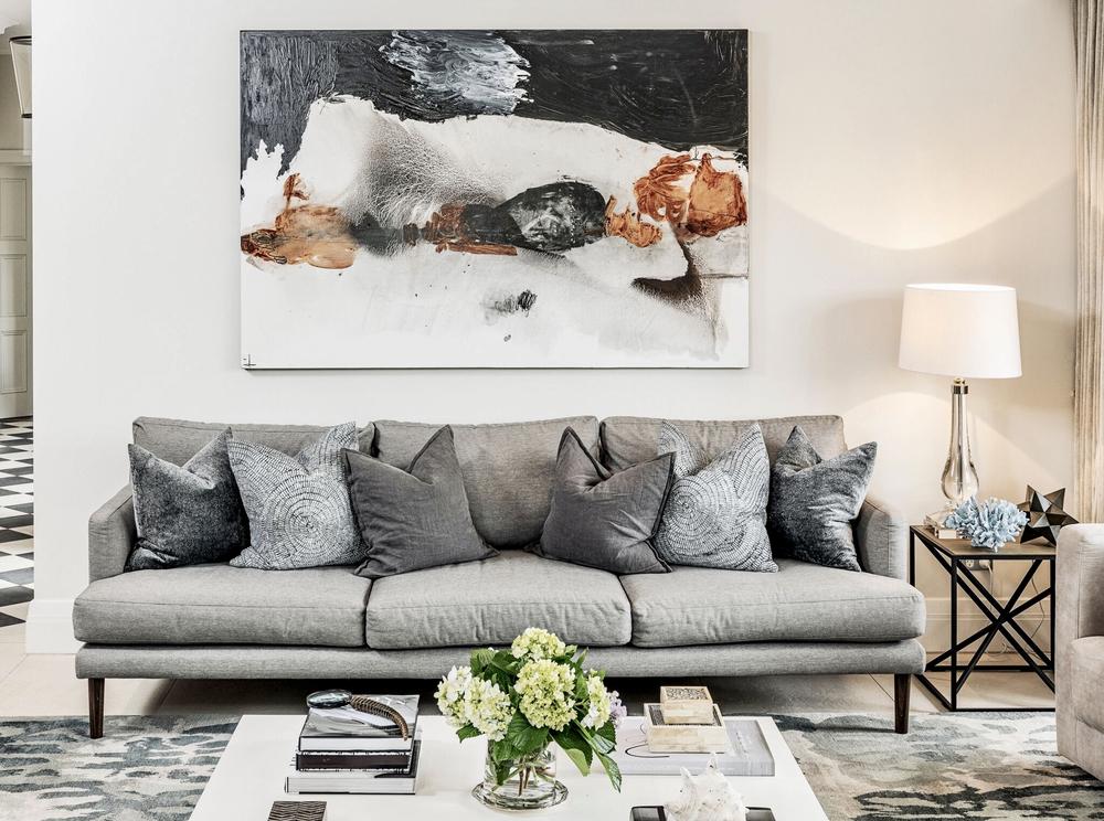 Grey upholstered sofa with patterned cushions beneath abstract artwork