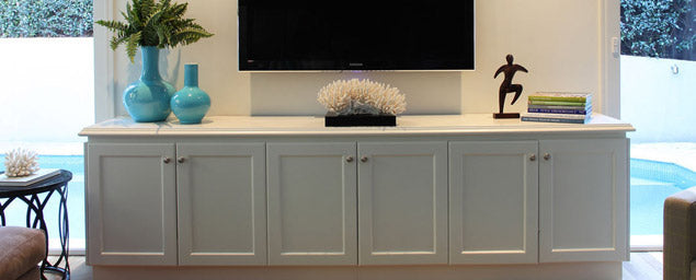 Pale fitted cabinet with decorative objects and a television above