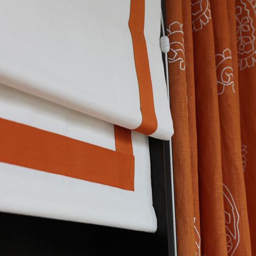 White fabric blind with orange border beside coordinating curtains