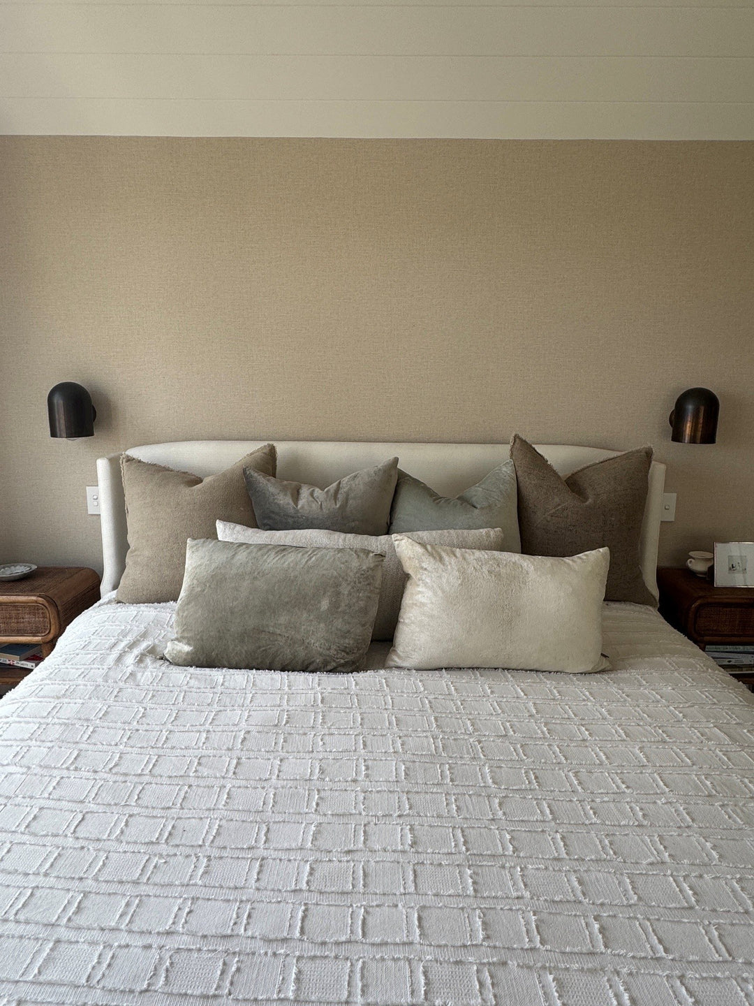 Neutral upholstered bedhead with layered cushions and bedside wall lights