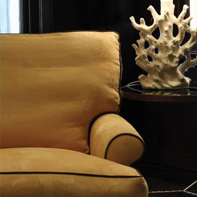 Mustard upholstered armchair with dark piping beside a round side table