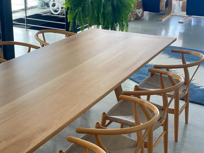 Pale timber dining table with curved-back timber chairs and woven seats