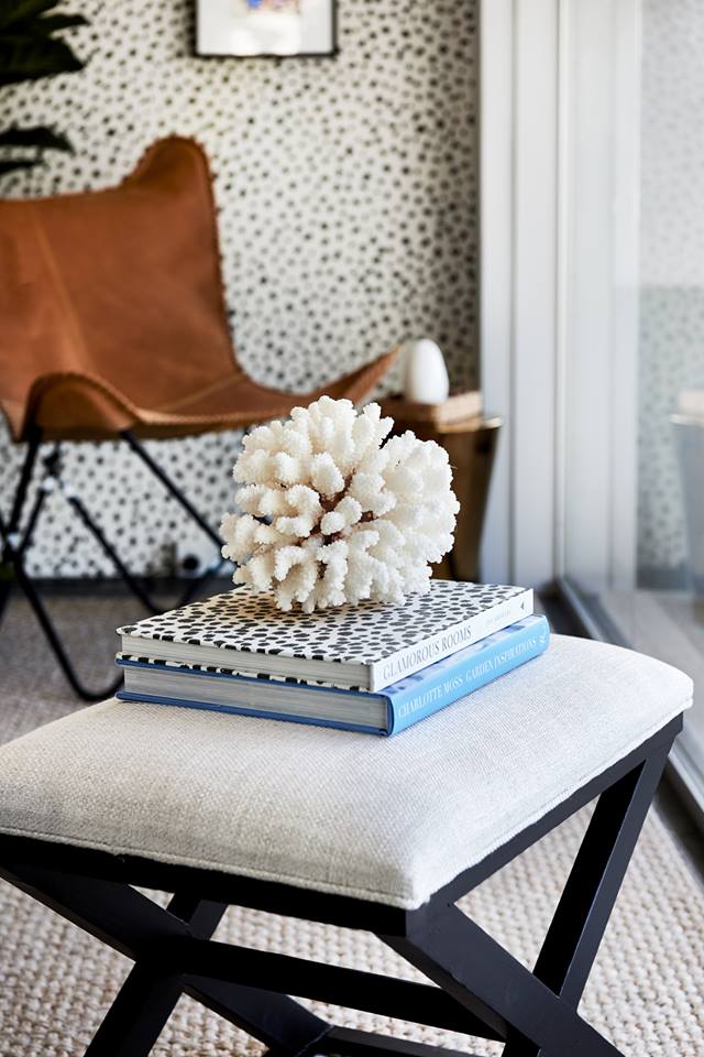Upholstered stool with books and a coral ornament beside a leather chair