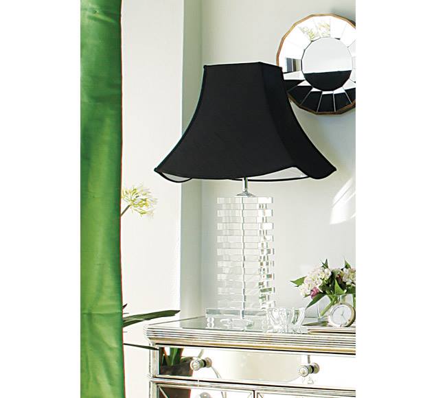 Table lamp with a curved reflective base and flared black shade beside green curtains