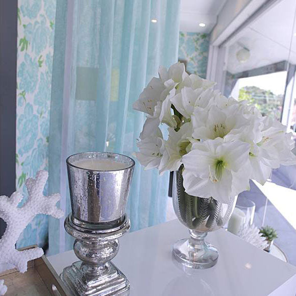 Pale patterned curtain beside flowers and a reflective side table