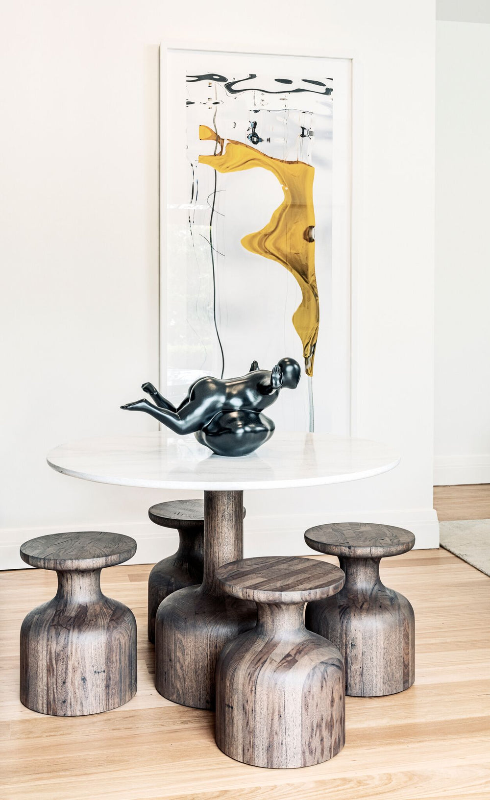 Round dining table with sculptural timber stools and framed artwork