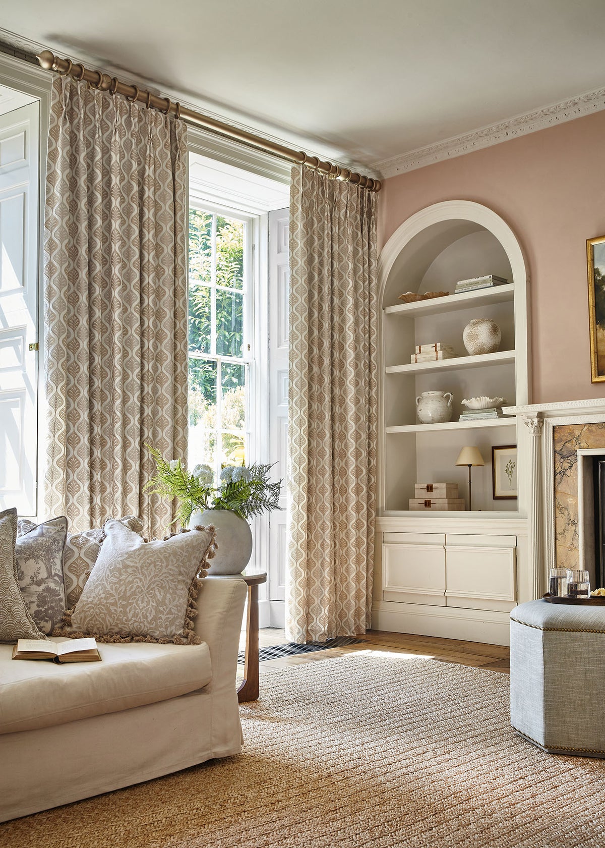 Patterned neutral curtains frame a tall window beside a cream sofa and built-in shelves.