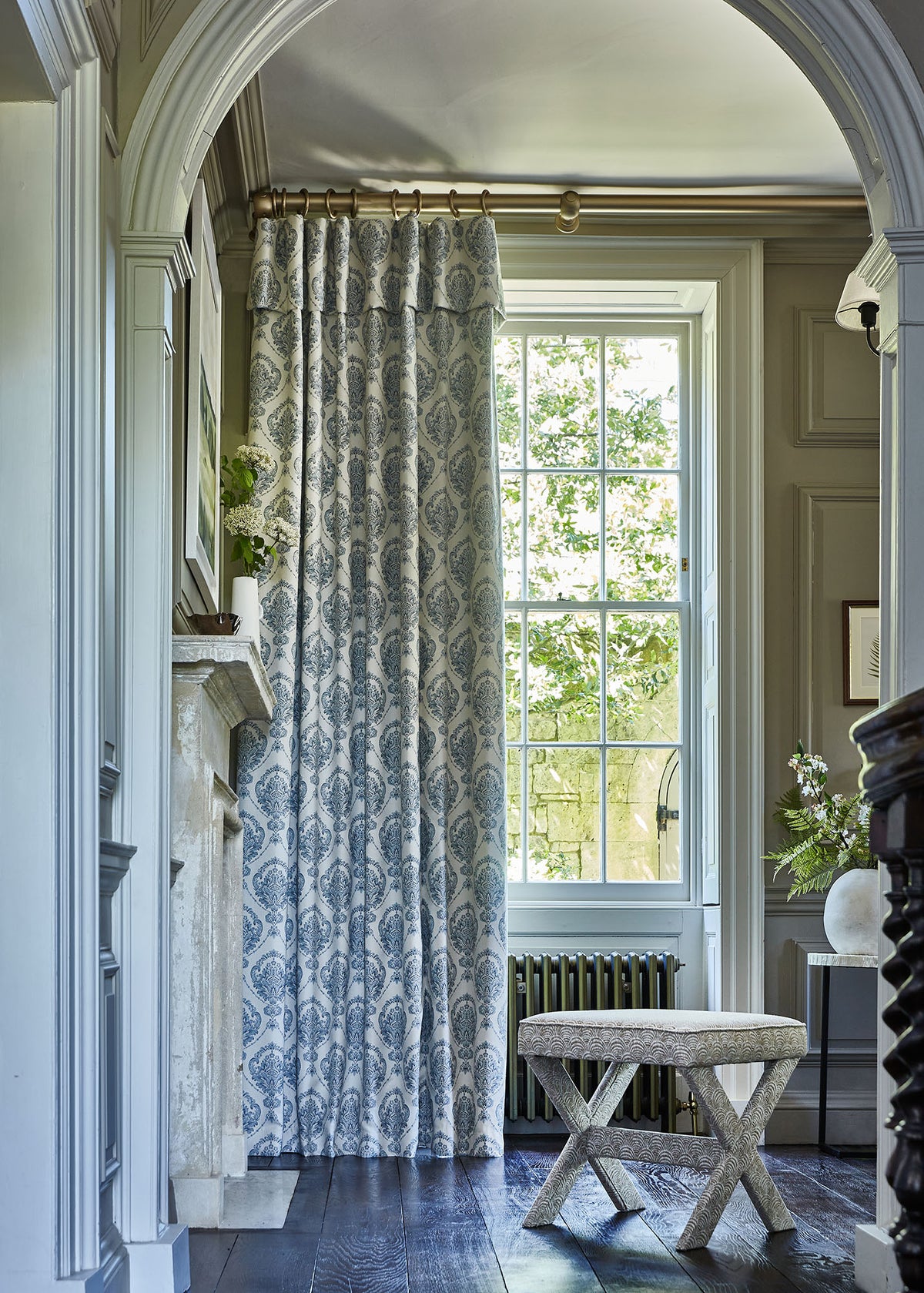 Blue patterned full-length curtain beside a small upholstered cross-leg stool.