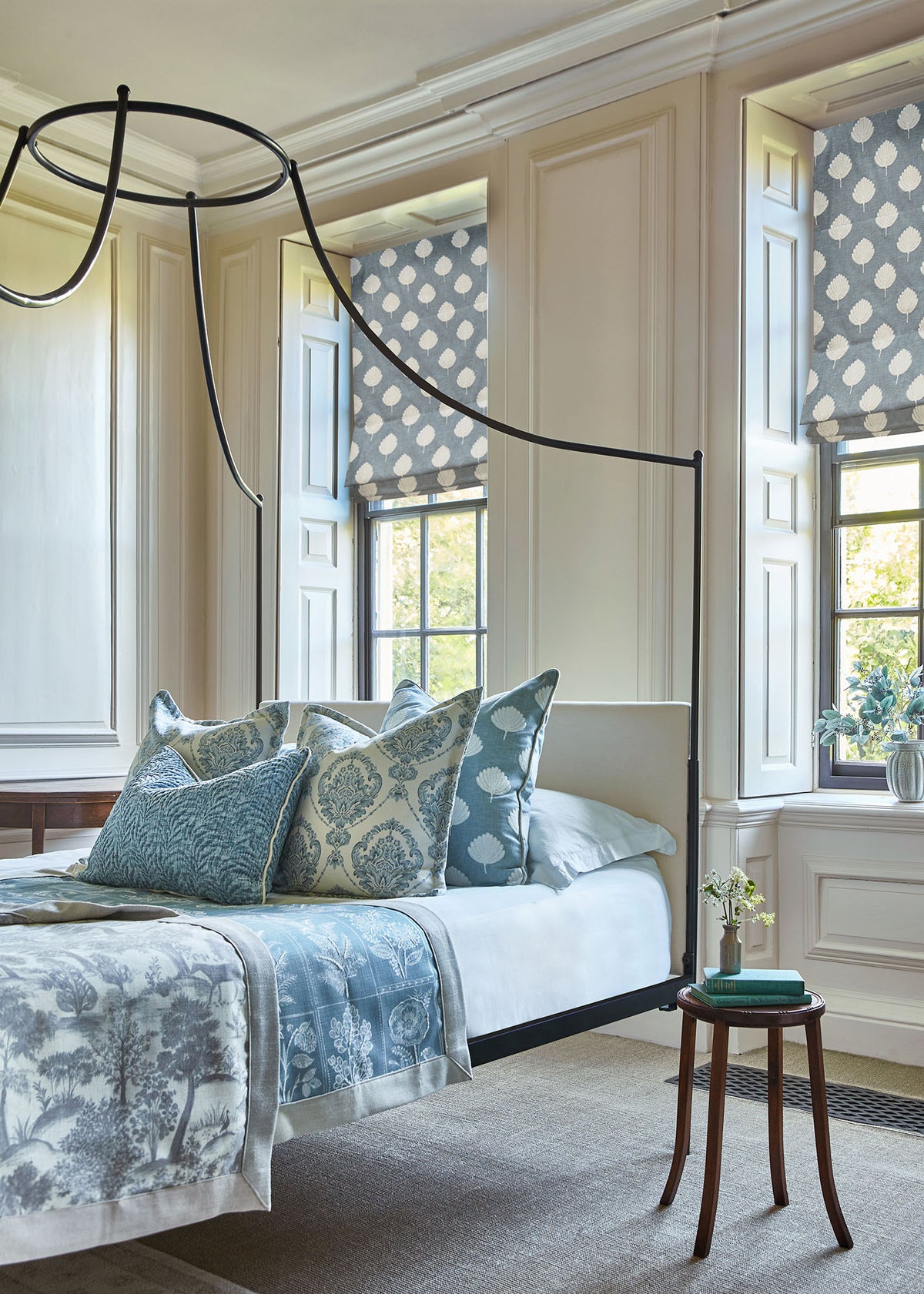 Bedroom with a pale upholstered bedhead, blue patterned cushions and bedding, and coordinating Roman blinds.