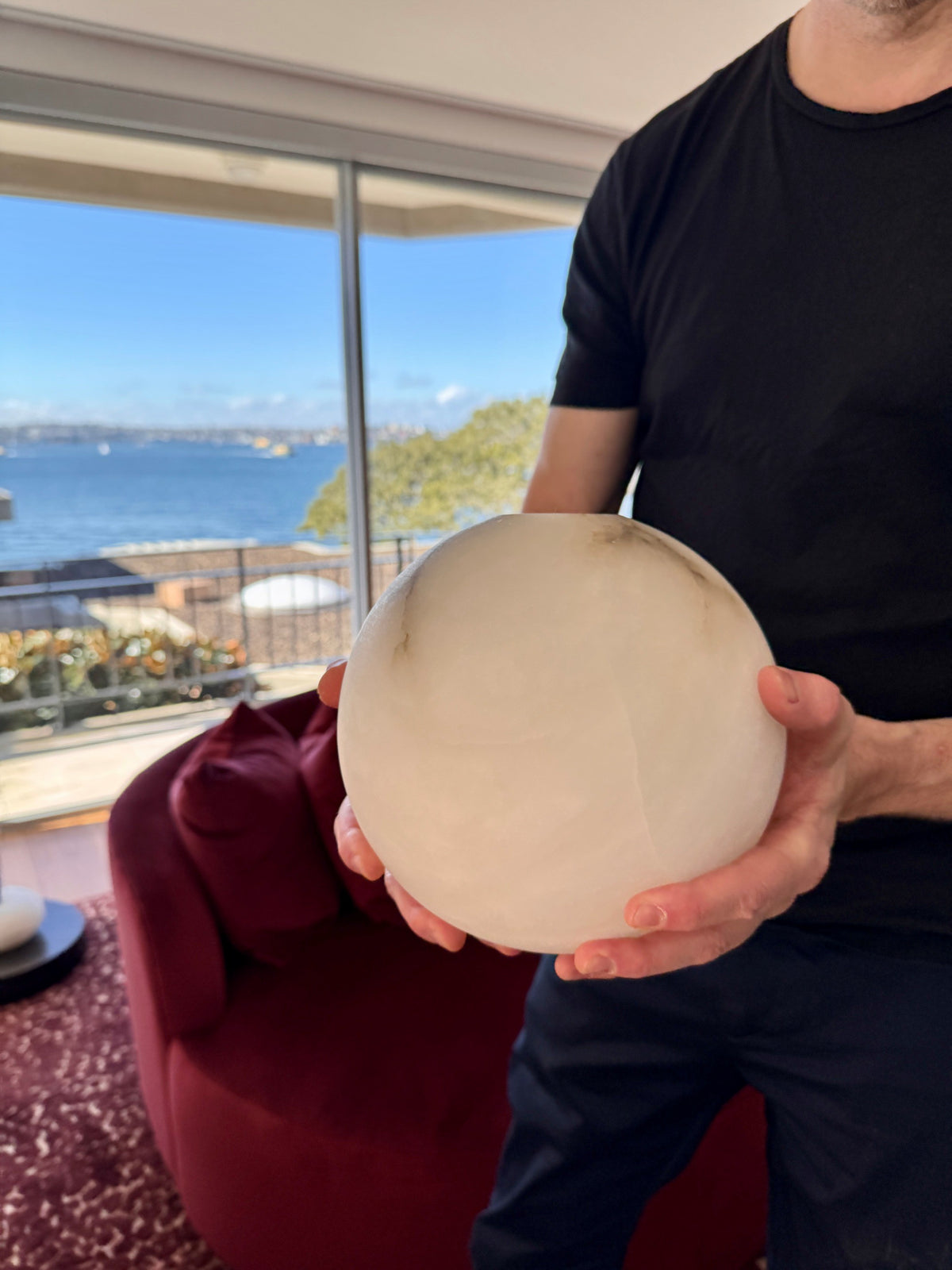 Person holding a pale rounded lamp component in a room overlooking the water