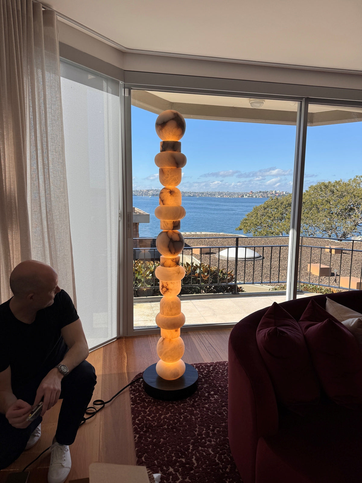 Tall illuminated floor lamp with stacked rounded forms beside a curved window and red seating