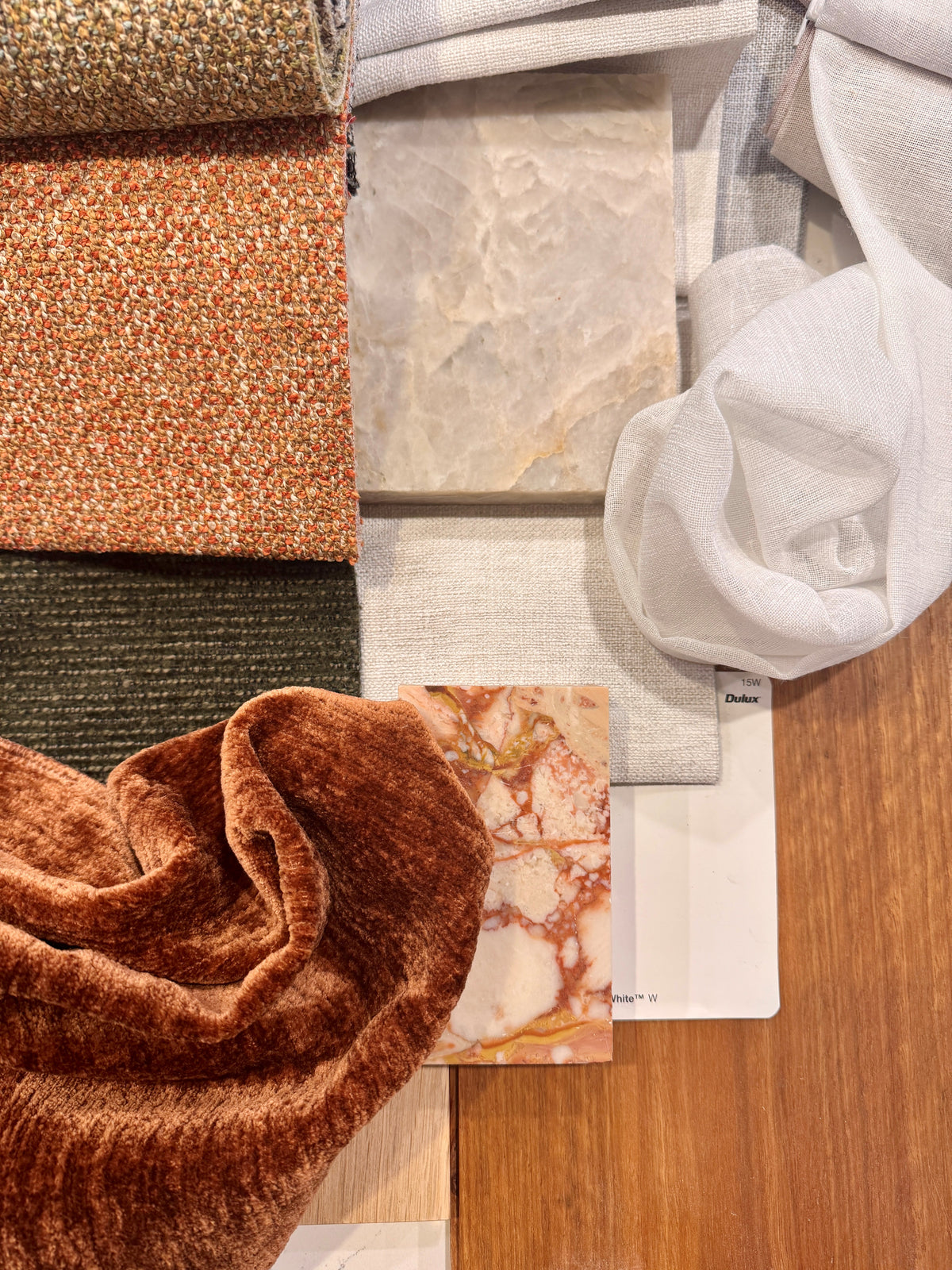 Orange, olive and cream fabric and finish samples arranged on a timber surface