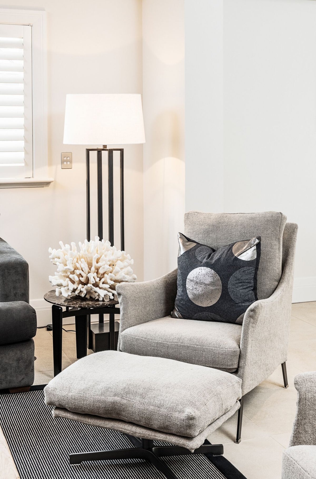 Pale armchair beside a floor lamp and louvred shutters