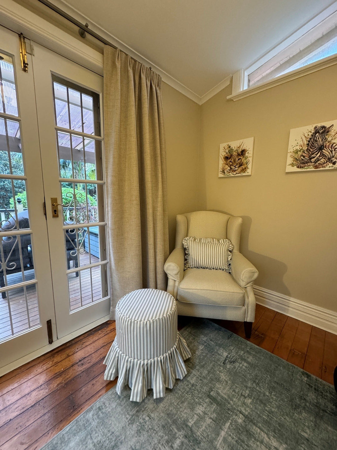 Pale armchair and blue striped skirted ottoman beside French doors