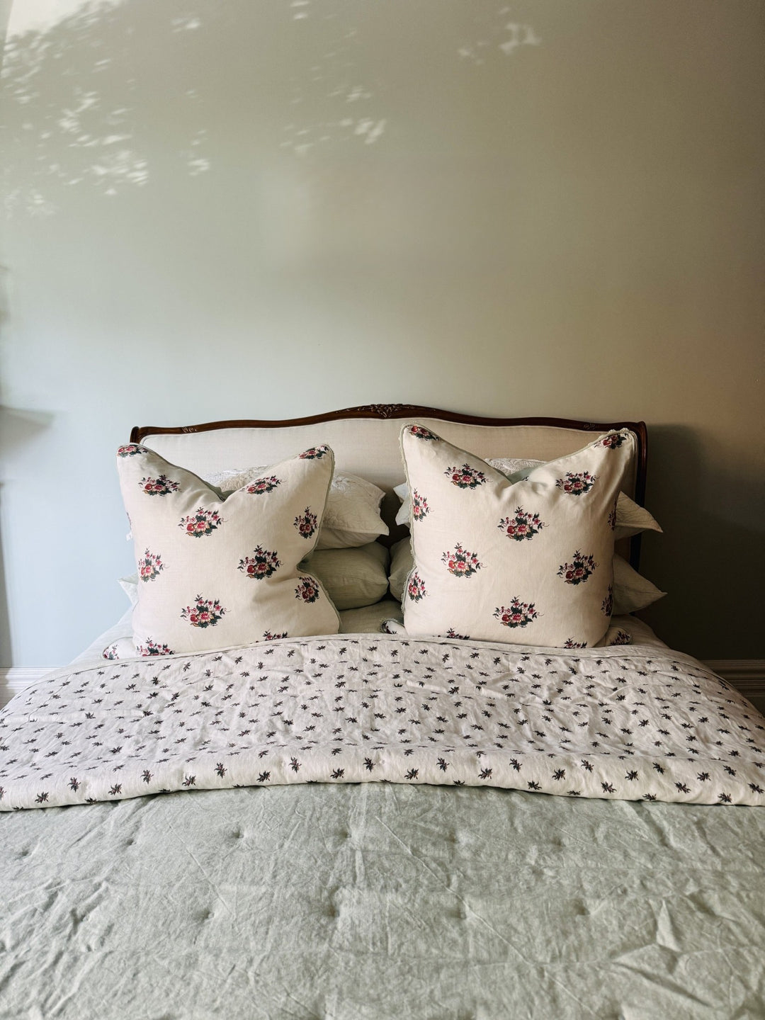 Soft green bedding and floral cushions on a timber-framed bed