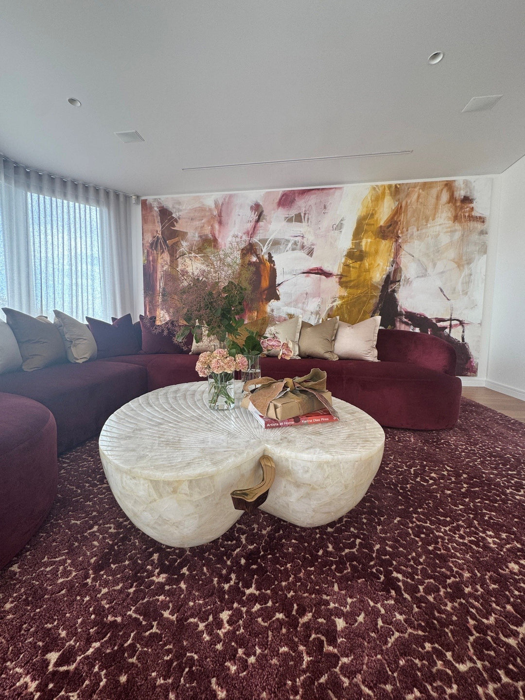 Rose-coloured curved sofa, pale coffee tables and expressive wallpaper in a living room